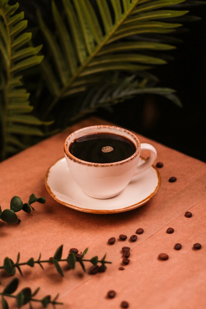 A warm espresso shot in a white cup, surrounded by coffee beans and lush green plants.